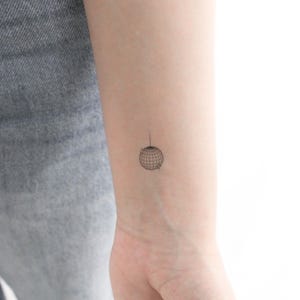 Könnte beinhalten: Eine kleine, schwarze Linienzeichnung eines Globus auf dem Handgelenk einer Person.