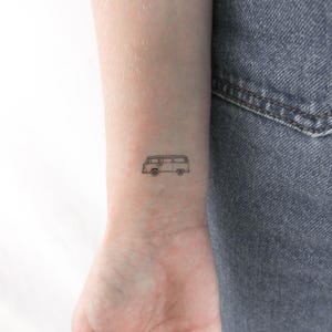 May include: A simple line drawing tattoo of a vintage van on a person's wrist.
