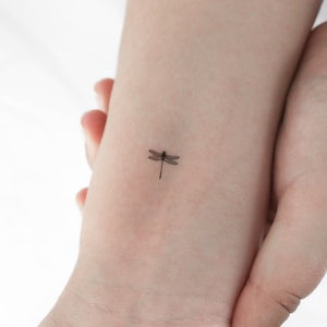 May include: A small, delicate dragonfly tattoo on a person's wrist.
