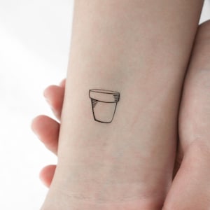 Puede incluir: Un simple dibujo de línea negra de una maceta en la muñeca de una persona.