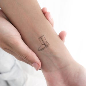 May include: A simple line drawing tattoo of a winter boot on a person's wrist.