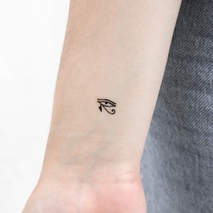 May include: A black and white temporary tattoo of the Eye of Horus, an ancient Egyptian symbol.