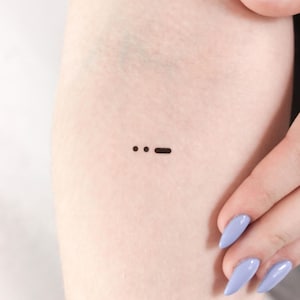May include: A small black tattoo of three dots and a dash on a person's arm.