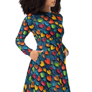 May include: A long-sleeved midi dress with a dark blue background and a colorful heart pattern. The dress has pockets on the sides.