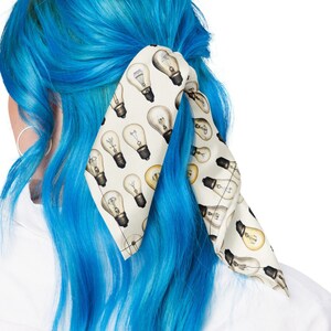 May include: A light blue hair scarf with a white background and a pattern of light bulbs. The scarf is tied around a ponytail.