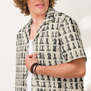 May include: A man wearing a beige button-up shirt with a black and white chess piece pattern. The shirt has a collar and short sleeves.