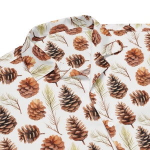 May include: A white button-up shirt with a brown and white pine cone pattern. The shirt has a collar and short sleeves.