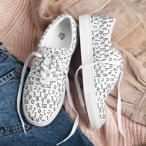 May include: White canvas sneakers with black letters printed all over the shoes. The letters are in a vintage font style.