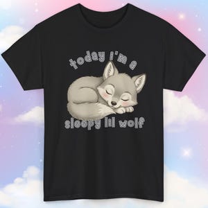 May include: Black t-shirt featuring a sleeping gray wolf illustration with the text "today i'm a sleepy lil wolf" in white. The wolf is curled up with its eyes closed, and the shirt has short sleeves.