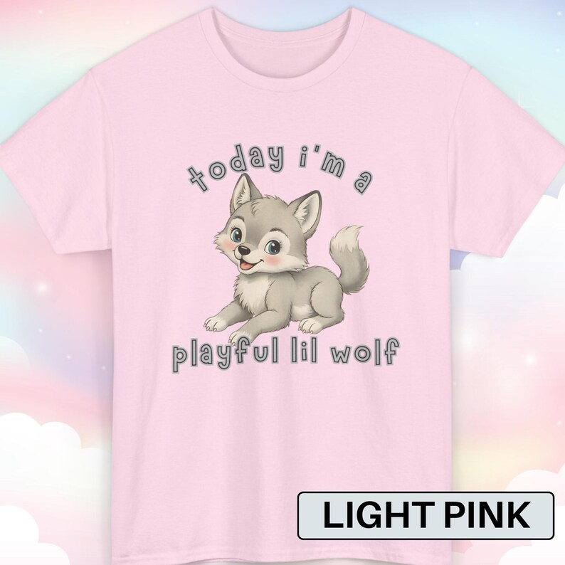 以下が含まれることがあります： 漫画のオオカミのイラストが描かれたライトピンクのTシャツ。オオカミはグレーと白で、フレンドリーな表情をしています。シャツのテキストは「today I'm a playful lil wolf」と書かれています。シャツの下部には「LIGHT PINK」という文字があります。