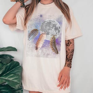 May include: A white t-shirt with a graphic print of three pill bugs on a watercolor background with a moon in the center. The pill bugs are facing the moon and appear to be reaching for it.