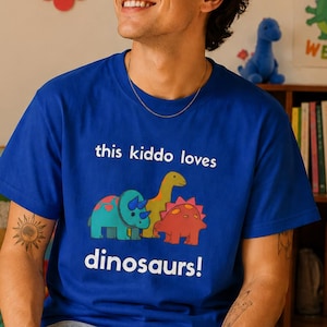 May include: A royal blue t-shirt with the text "this kiddo loves dinosaurs!" and a graphic of three cartoon dinosaurs in teal, yellow, and red. The shirt is short-sleeved.