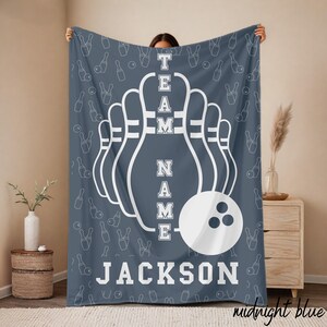 May include: A midnight blue blanket featuring a bowling theme. The design includes white bowling pins, a bowling ball, and the text "TEAM NAME JACKSON". The background has a pattern of bowling pins and bowling balls.
