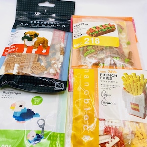 May include: Several packages of Nanoblock mini building block sets. The sets include a dog, a hot dog, a bird, and french fries. The packages are in various colors, including brown, yellow, and green.