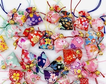 May include: A collection of small fabric pouches featuring various floral patterns in red, pink, blue, yellow, and black. Each pouch is cinched at the top with a colorful cord and includes a small, round, gold-toned metal bell attached to the string.