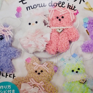 May include: A set of five plush toy kits for making small teddy bears. The kits include all the materials needed to create a pink, white, brown, green, and purple teddy bear. The bears are wearing pink, white, and green bows. The packaging includes the text "moru doll kit" and "make it cute".