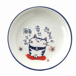 May include: A white ceramic plate with a blue rim. The plate features a cartoon cat illustration in blue and white, sitting on a red cushion. Japanese text is also present.