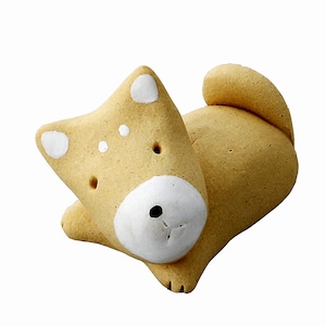 May include: A small, ceramic dog figurine in a light brown colour with white accents. The dog is lying down with its head resting on its paws.