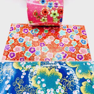 May include: A roll of decorative tape with a pink floral pattern, measuring 1.96 inches wide and 39.3 inches long. The image also shows samples of the tape's designs: a red background with colorful flowers and a blue background with gold accents and white flowers.