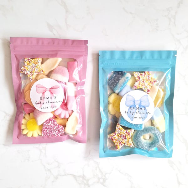 May include: Two stand-up pouches filled with assorted gummy candies. The left pouch is pink with a sticker featuring a pink bow and the text 'EMMA'S baby shower 23.04.2025'. The right pouch is blue with a sticker featuring a blue bow and the same text.