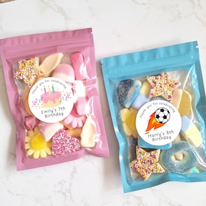 May include: Two clear plastic bags filled with colorful candies. One bag is pink and features a sticker that reads "Emily's 7th Birthday." The other bag is blue and has a sticker that says "Harry's 8th Birthday."