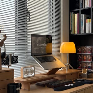 May include: A laptop computer with a wooden stand, a lamp, and a keyboard on a wooden desk. The laptop screen displays the word "essential".