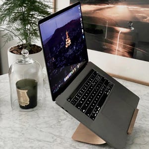 May include: A silver laptop computer with a black keyboard is elevated on a wooden stand. The laptop is open and the screen shows a night time cityscape. The laptop is on a white marble surface.