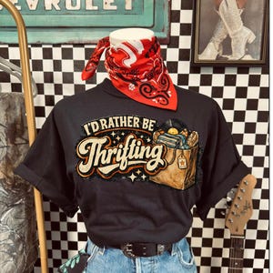 Peut inclure: T-shirt noir avec l'inscription "I'd Rather Be Thrifting" et un graphisme d'une bo&icirc;te remplie de disques vinyles. Le t-shirt est associ&eacute; &agrave; un jean bleu, un bandana rouge et une ceinture noire. Une guitare et une enseigne vintage sont en arri&egrave;re-plan.