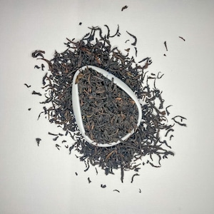 Puede incluir: Hojas sueltas de té negro en un cuenco de cerámica blanco, esparcidas sobre un fondo blanco.