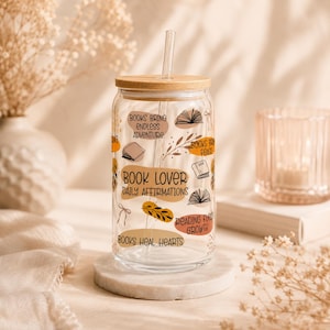 Puede incluir: Un vaso de vidrio transparente con tapa de bambú y pajita de vidrio, con ilustraciones y textos impresos que incluyen libros, hojas y cintas. El texto dice: Books bring endless adventure, Books bring peace, Book lover daily affirmations, Reading fuels growth y Books heal hearts.