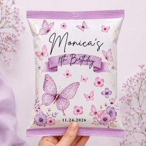May include: A rectangular snack bag with a white background featuring purple butterflies and floral illustrations. The text reads Monica's 11th Birthday and 11.24.2026. The bag has a light purple scalloped top and bottom edge with a central purple ribbon.