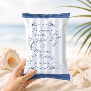 May include: A rectangular snack bag with a light blue and white vertical striped pattern. The bag features dark blue text reading The summer I TURNED fifteen Monica's 15th Birthday 11.24.2026, decorated with illustrations of seashells and starfish.