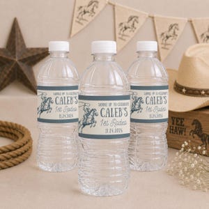 May include: Three clear plastic water bottles with white caps, each featuring a blue and cream label. The label displays a graphic of a cowboy on a horse with the text: SADDLE UP TO CELEBRATE CALEB'S 1st Rodeo 11.24.2026 in dark blue lettering.