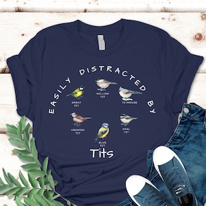 May include: A navy blue t-shirt with a white graphic of different types of birds with the text "EASILY DISTRACTED BY Tits".