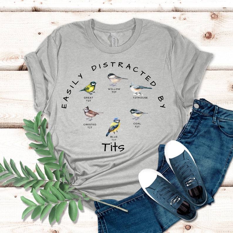 May include: A gray t-shirt with the text "Easily Distracted By Tits" and illustrations of different types of birds, including a great tit, crested tit, willow tit, titmouse, coal tit, and blue tit.