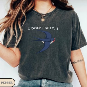 May include: A dark gray t-shirt with a white swallow graphic and the text "I don't spit I" printed on the front.