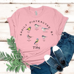 May include: Pink t-shirt with the text "Easily Distracted By" and a circle of different types of birds with the text "Tits" underneath.