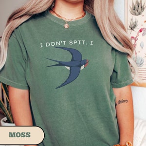 May include: A moss green t-shirt with the text "I don't spit. I" and a blue swallow illustration.