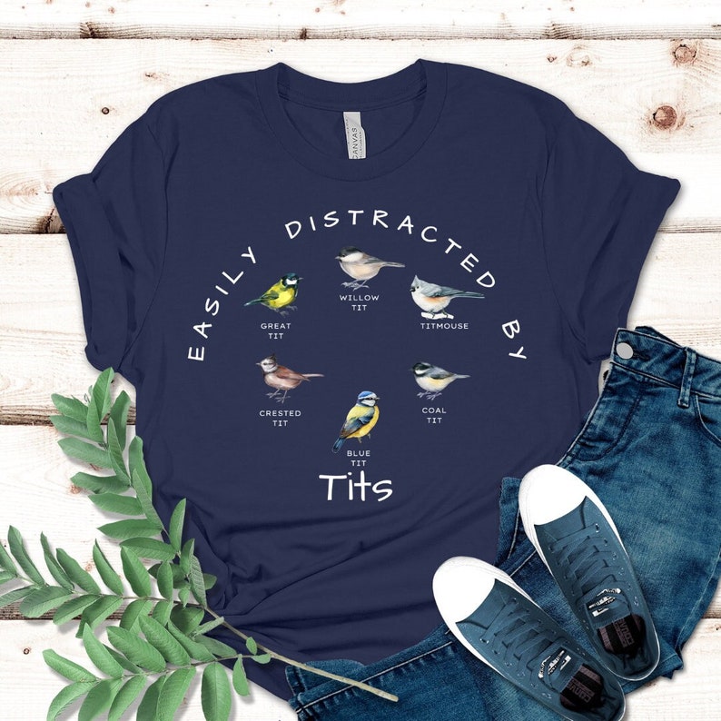May include: A navy blue t-shirt with a white graphic of different types of birds with the text "EASILY DISTRACTED BY Tits".