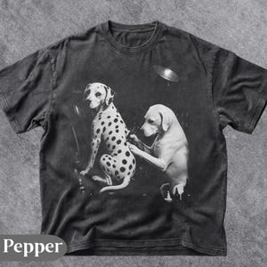 Könnte beinhalten: Dunkelgraues T-Shirt mit einer Schwarz-Weiß-Grafik von zwei Hunden. Einer ist ein Dalmatiner, der von einem anderen Hund tätowiert wird. Das Wort "Pepper" ist unten auf dem Shirt aufgedruckt.