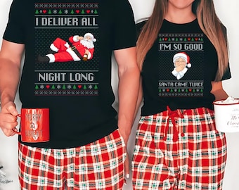 May include: Matching Christmas outfits featuring black t-shirts and red plaid pajama pants. One shirt reads "I DELIVER ALL NIGHT LONG" with a Santa graphic. The other shirt says "I'M SO GOOD SANTA CAME TWICE" with a Santa graphic. A red mug with "MERRY & BRIGHT" is visible.