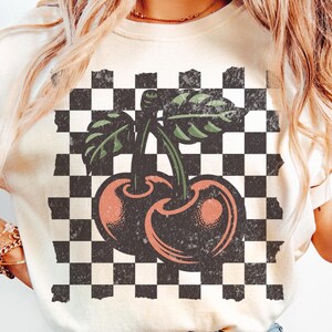 Studio shot of checkered cherries t-shirt – bold cherry pattern on a Comfort Colors vintage tee, perfect for 90s and Y2K fashion lovers. Ivory, vintage white color.