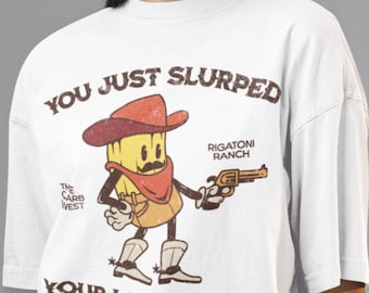 Könnte beinhalten: Ein weißes Kurzarm-T-Shirt mit einer Grafik einer Rigatoni-Nudel im Cowboy-Stil mit Schnurrbart, Hut und Pistole. Der Text lautet: YOU JUST SLURPED YOUR LAST NOODLE, THE CARB WEST, RIGATONI RANCH, COWBOYS, CARBS, & CHAOS.