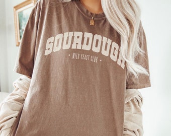 May include: An oversized brown t-shirt with the text "SOURDOUGH WILD YEAST CLUB" printed in white. The model is wearing size XL for an oversized fit. She normally wears size M for a regular fit.