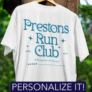 May include: White t-shirt featuring the teal text "Prestons Run Club". The design includes stars, the words "ESTD 2026" and "WE'RE HERE FOR THE LONG RUN". The bottom of the shirt reads "PERSONALIZE IT!"