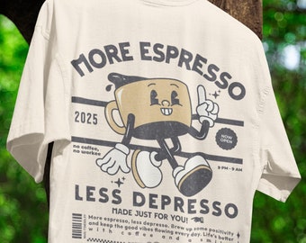 May include: Cream-colored t-shirt with a cartoon coffee cup graphic. The design includes the text "MORE ESPRESSO" and "LESS DEPRESSO." The graphic features a coffee cup character with arms and legs, pointing upwards. Additional text includes "MADE JUST FOR YOU!" and "NOW OPEN."