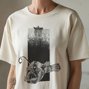 Hand-drawn anglerfish tee featuring a deep ocean scene with a boat and fisherman on the surface. Perfect for nature lovers, fans of retro 90s and 2000s style, and grunge fashion enthusiasts. Fish Shirt.