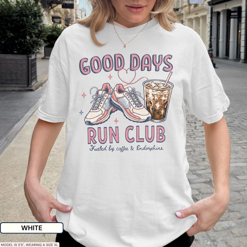 May include: A white t-shirt featuring a graphic print with the text GOOD DAYS RUN CLUB and Fueled by coffee & Endorphins. The design includes a pair of athletic sneakers, a glass of iced coffee with a straw, and a thin red heart outline.