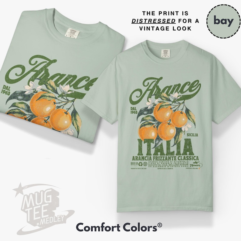 May include: Two light green t-shirts with a vintage-style graphic. The graphic features the word "Arance" in a distressed green font, with orange fruit and the word "Italia" below. The text "THE PRINT IS DISTRESSED FOR A VINTAGE LOOK" is above.