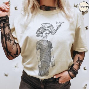 Comfort Colors® ivory T-shirt featuring Prakash’s hand-drawn line-art figure; styled with mesh sleeves and butterflies backdrop to show print scale and everyday wear.